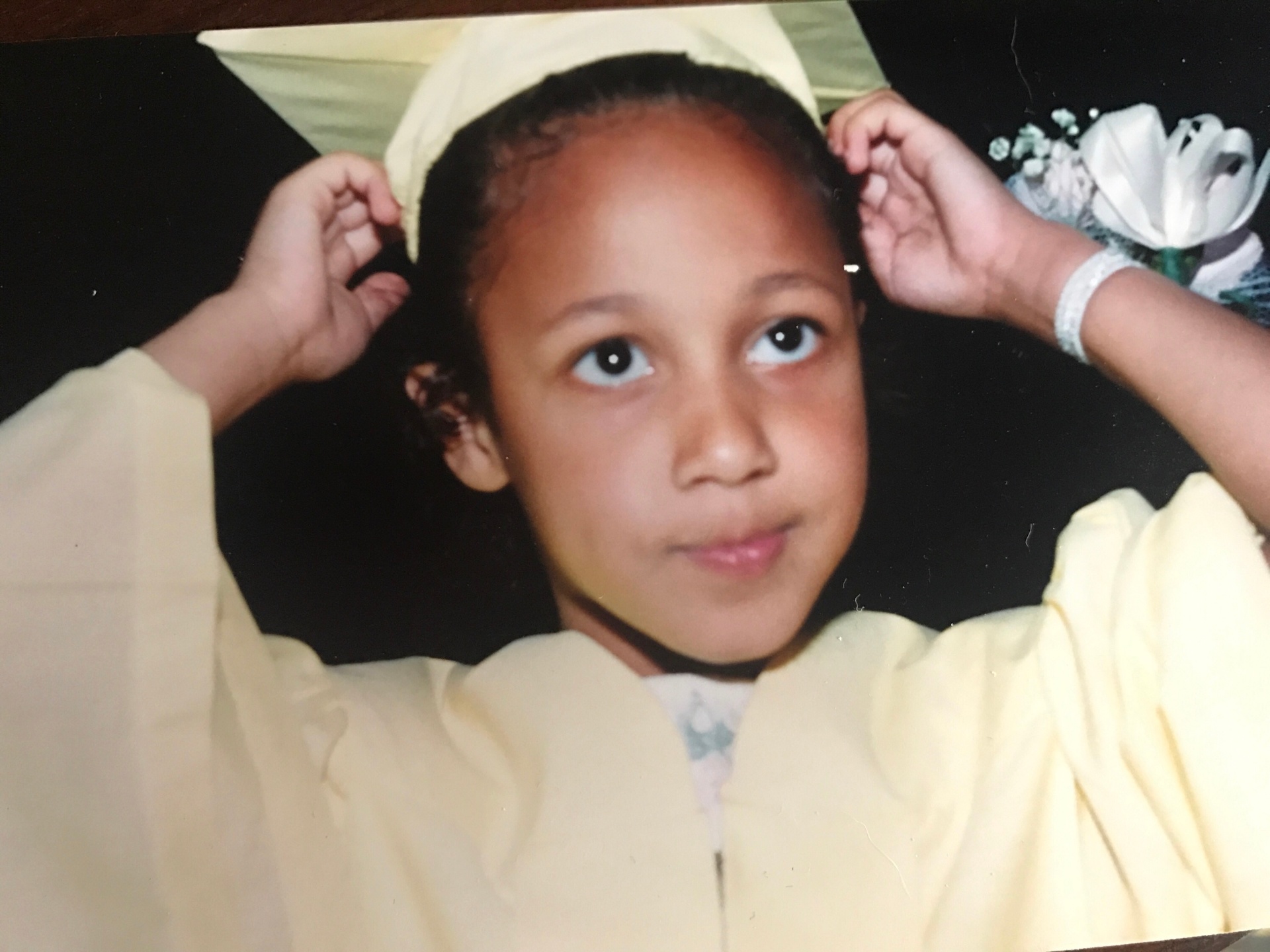 Cynthia as a child in a yellow graduation cap and gown